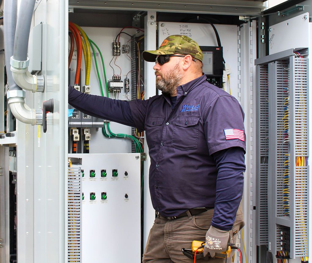 Willis Mechanical technician with a multimeter at an open control cabinet full of color-coded wiring