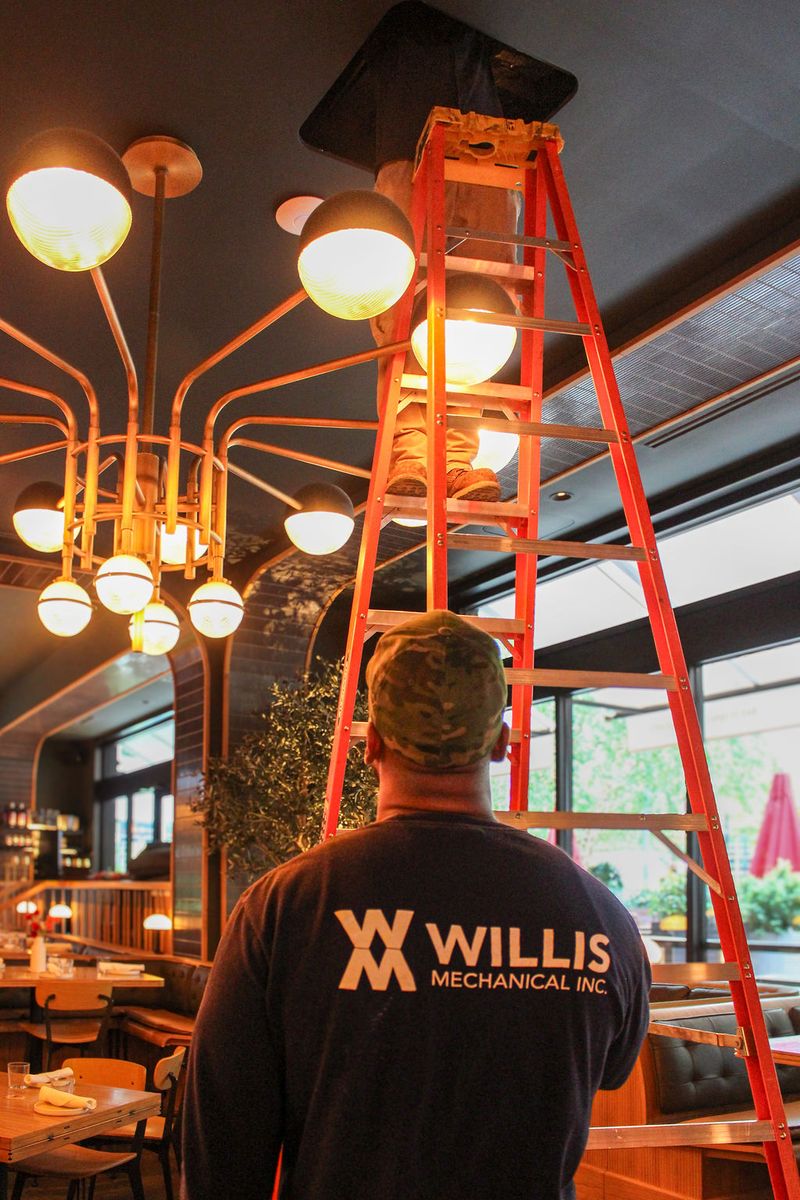 Technician footing a ladder while a second technician works inside a ceiling access panel