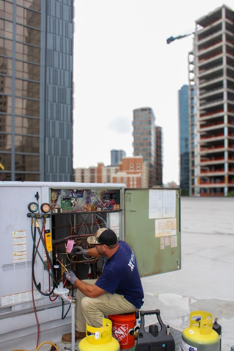 Technician working inside a rooftop unit with the downtown skyline and a tower crane above