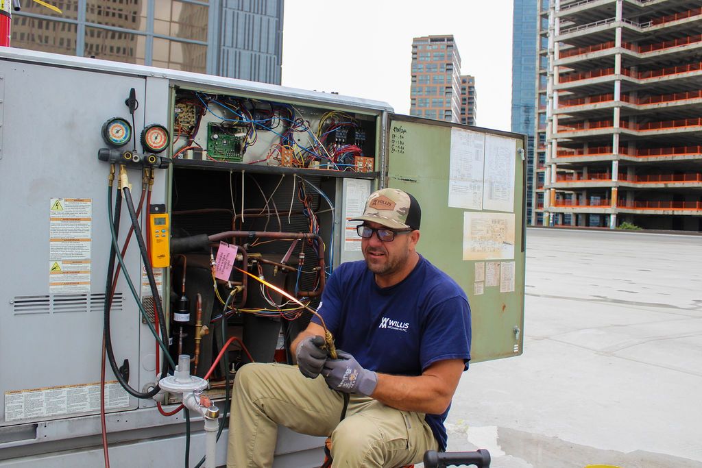 Technician brazing a refrigerant line on a rooftop unit with the Atlanta skyline behind