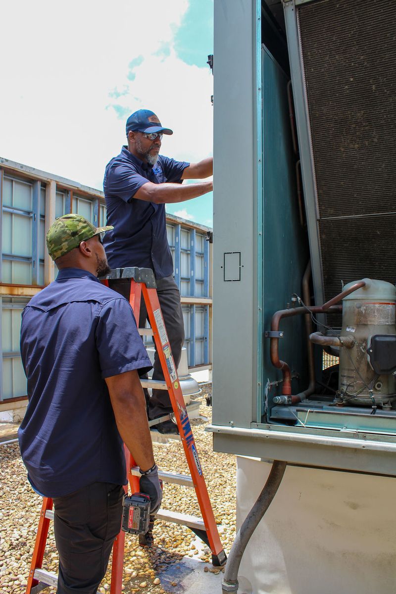 Technician on a ladder reaching into an open condensing unit