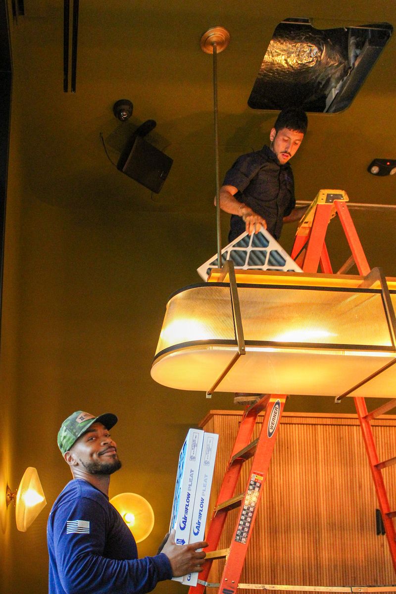 Two technicians passing filters up a ladder inside a restaurant