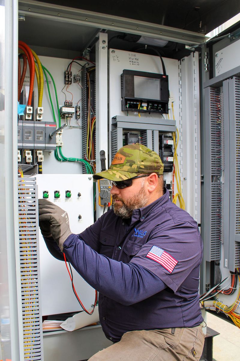 Technician probing wiring inside a control cabinet with a multimeter