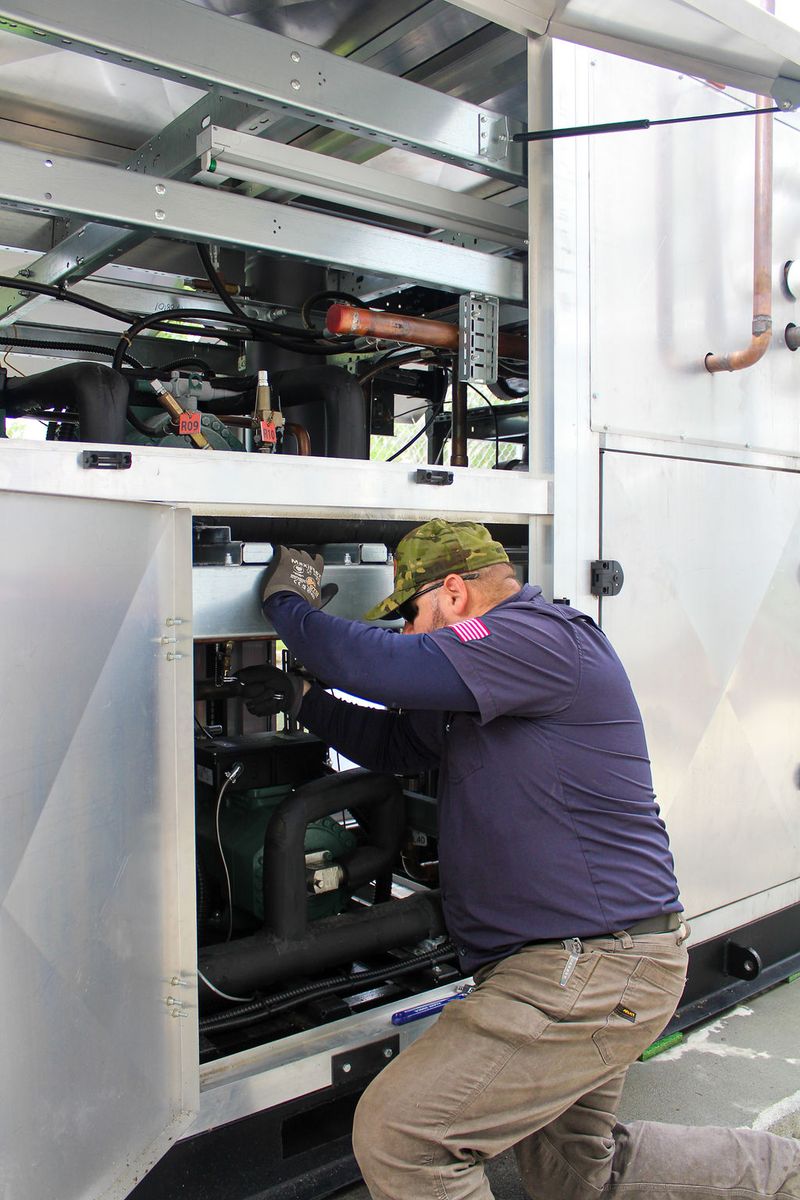Technician reaching into an open compressor compartment on an outdoor refrigeration skid